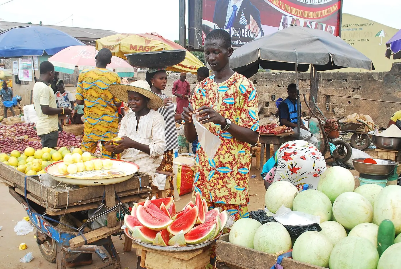 A fruit seller with oranges and melons at a busy market